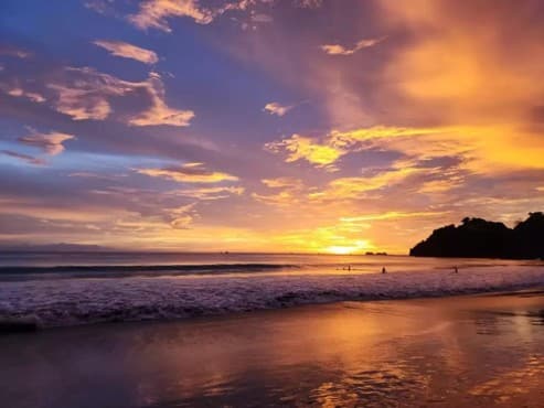 Atardecer de intensos tonos naranja y morado sobre el mar, con una isla rocosa en el horizonte