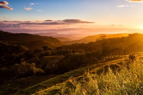 Luz dorada del atardecer sobre montañas onduladas cubiertas de bosque y laderas de pasto