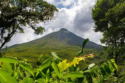 Volcán de forma cónica que se eleva sobre el bosque lluvioso verde bajo un cielo parcialmente nublado