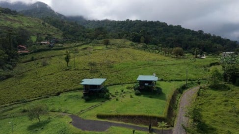 Pequeñas cabañas en potreros verdes de una ladera rodeada de montañas boscosas