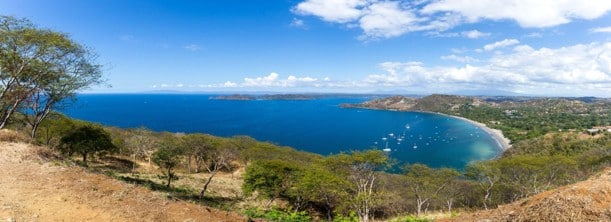 Vista panorámica de una bahía azul y tranquila con embarcaciones, vista desde una ladera de bosque seco