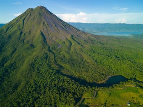 Vista aérea de un volcán en forma de cono cubierto de bosque junto a una laguna