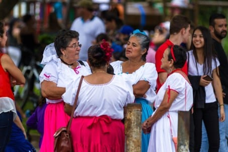 Grupo de personas, varias mujeres con blusas blancas tradicionales y faldas de colores, reunidas en un evento al aire libre