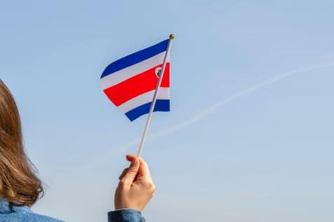 Mano sosteniendo una pequeña bandera de Costa Rica contra un cielo azul despejado