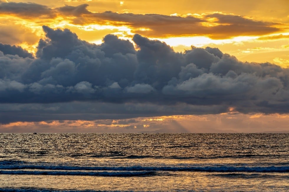 Nubes de tormenta sobre el mar al atardecer, con luz dorada reflejada en el agua