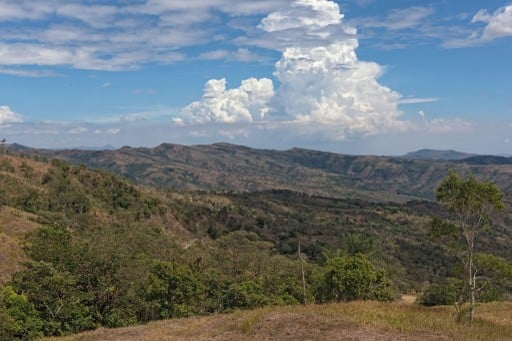Amplio paisaje de montaña con cordilleras boscosas y grandes nubes blancas en un cielo azul