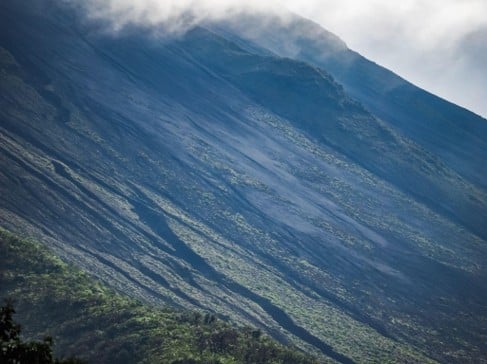 Ladera volcánica empinada de roca oscura y vegetación escasa que se eleva hacia las nubes