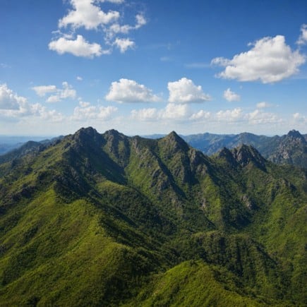 Picos montañosos verdes bajo un cielo azul con nubes blancas dispersas