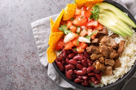 Tazón con arroz, frijoles rojos, trocitos de carne, pico de gallo, rodajas de aguacate y tortillas tostadas
