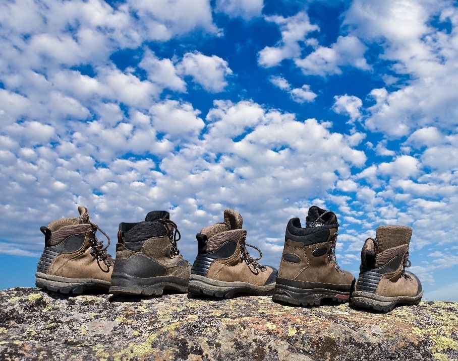 Fila de botas de montaña sobre una roca frente a un cielo azul lleno de pequeñas nubes