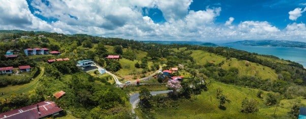 Vista aérea de un poblado en una ladera verde con casas de techos rojos cerca de un cuerpo de agua